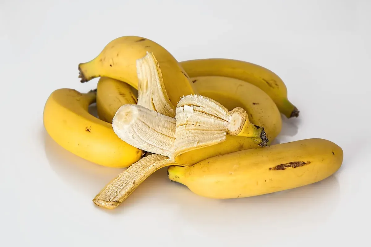 Bananas maduras sobre mesa branca, uma delas descascada