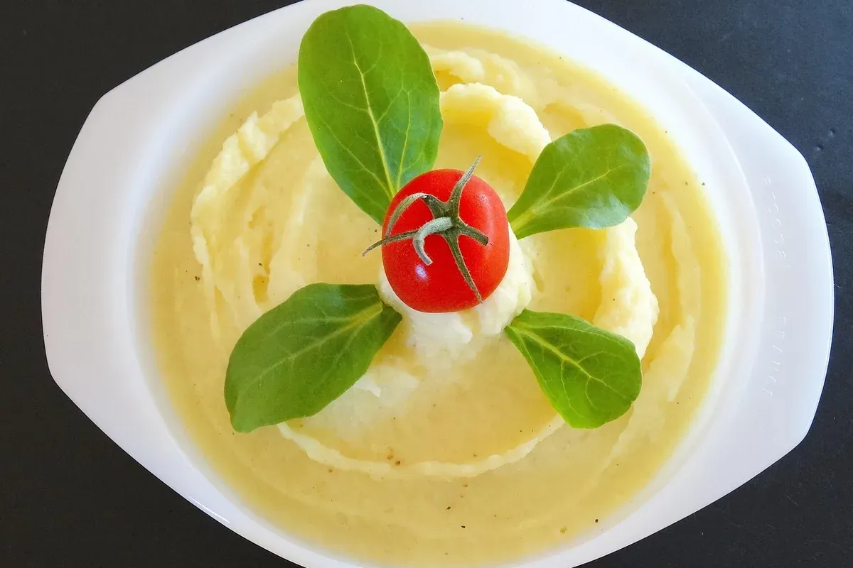 Purê de batata em travessa branca, com folhas verdes e um tomate cereja por cima