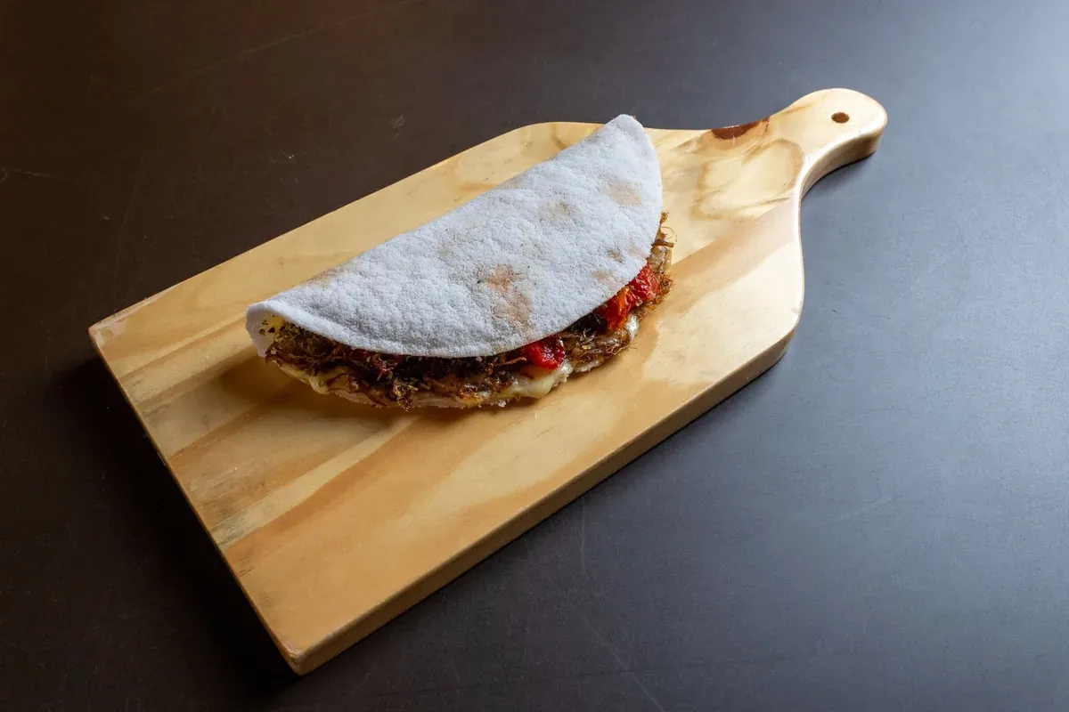 Tapioca recheada com carne desfiada, queijo e tomate sobre tábua de madeira